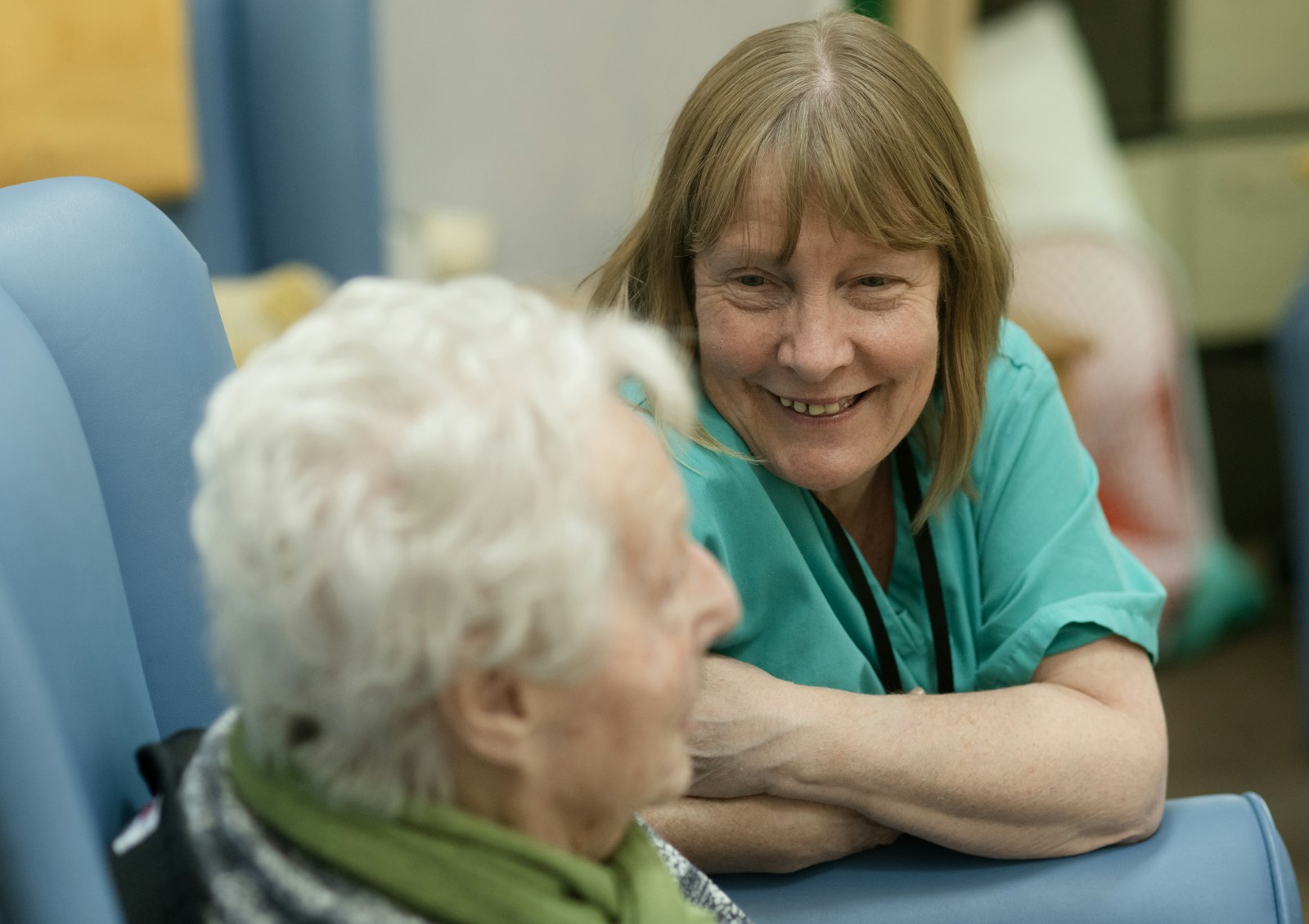 Carer in scrubs talking with an older woman in a care home
